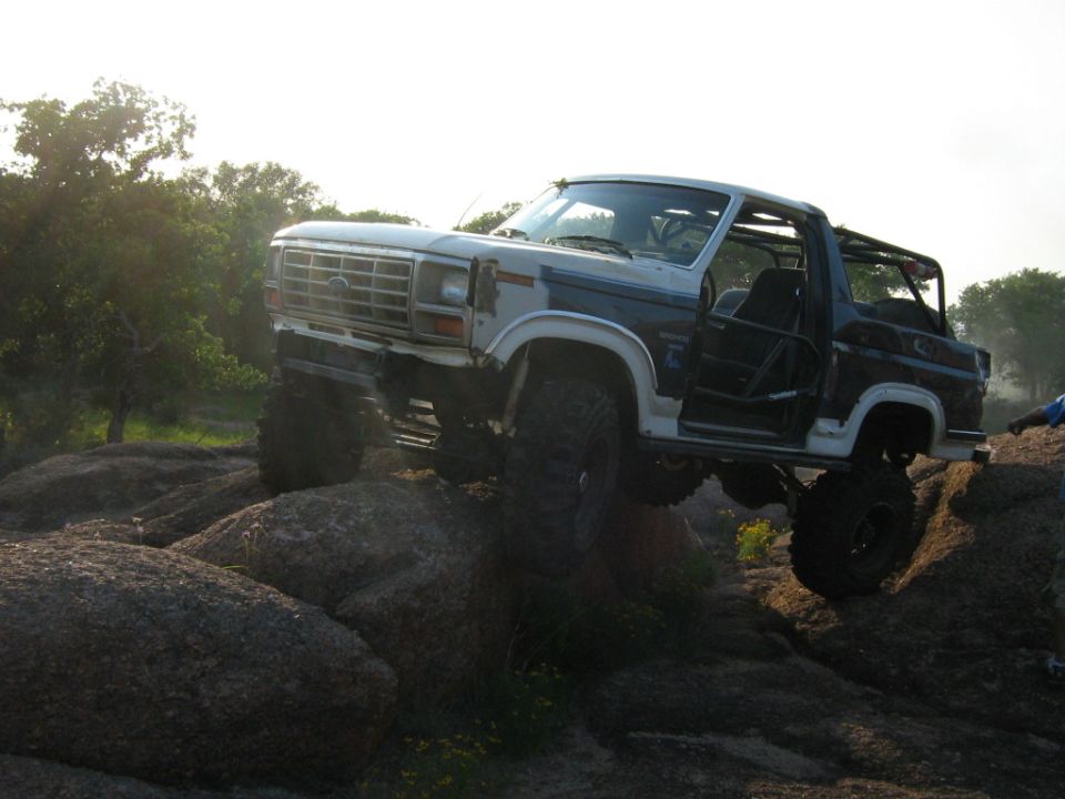 Lifted blue and white Ford Bronco with roll cage and no doors crawling over granite boulders
