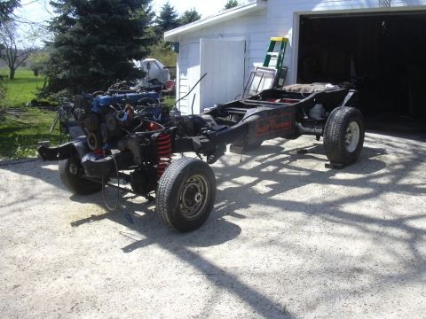 1996 Ford Crown Victoria - The vehicle's chassis and engine are exposed, with the body removed, in front of a garage.