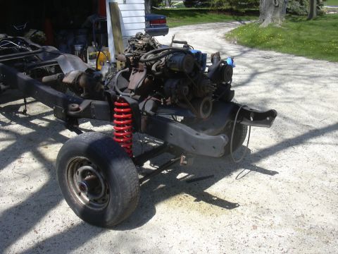 1996 Ford Crown Victoria - The chassis of a vehicle, with its engine and suspension components exposed, sits on a gravel surface.