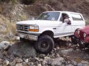 1994 Ford Bronco - White Ford Bronco navigating a rocky off-road trail with another vehicle nearby.