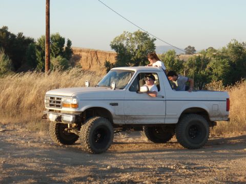 1994 Ford Bronco - A white 1994 Ford Bronco is seen off-road with several people riding inside and in the open bed.