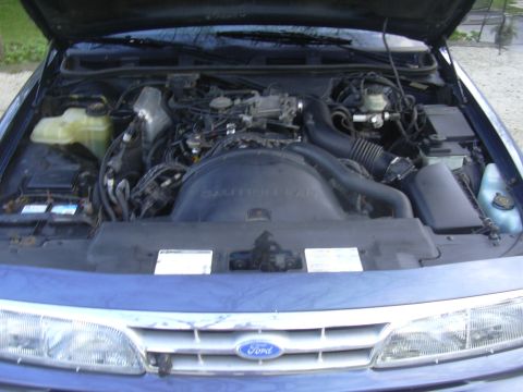1996 Ford Crown Victoria - The engine bay of a blue 1996 Ford Crown Victoria is shown with the hood raised, revealing the engine and surrounding components.