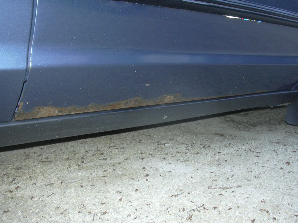 Blue car lower body panel showing rust damage along the rocker panel