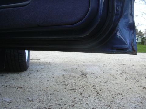 1996 Ford Crown Victoria - Close-up view of a car's door sill and tire, with a house visible in the background.