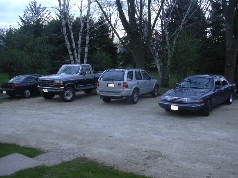 1996 Ford Crown Victoria - This dark blue sedan, likely a 1996 Ford Crown Victoria, is parked alongside other vehicles.