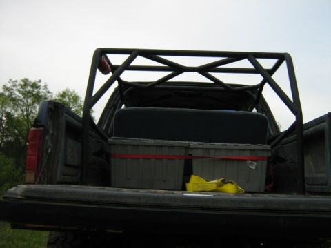 1986 Ford Bronco - The rear of a pickup truck bed is visible, equipped with a roll cage and two storage containers secured with red straps.