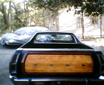 1973 Ford Ranchero - Wood-paneled Ford Ranchero rear view, with a second vehicle obscured by a cover.