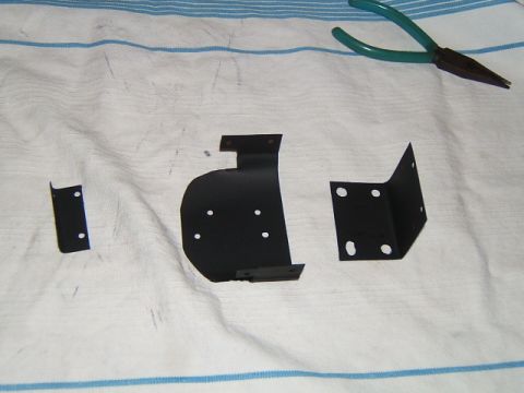 1988 Ford Bronco - Several black metal brackets and a pair of pliers are laid out on a white cloth with blue stripes.