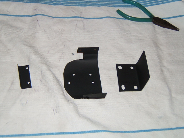 three black metal brackets and a pair of pliers on a striped cloth