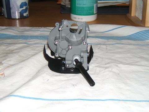 1988 Ford Bronco - A close-up view of a gray plastic gearbox assembly with a black metal bracket and output shaft.