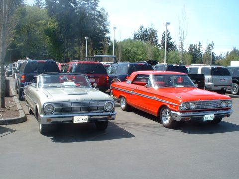 2000 Ford Crown Victoria - An orange 1964 Ford Galaxie hardtop is parked next to a silver convertible at a car show.