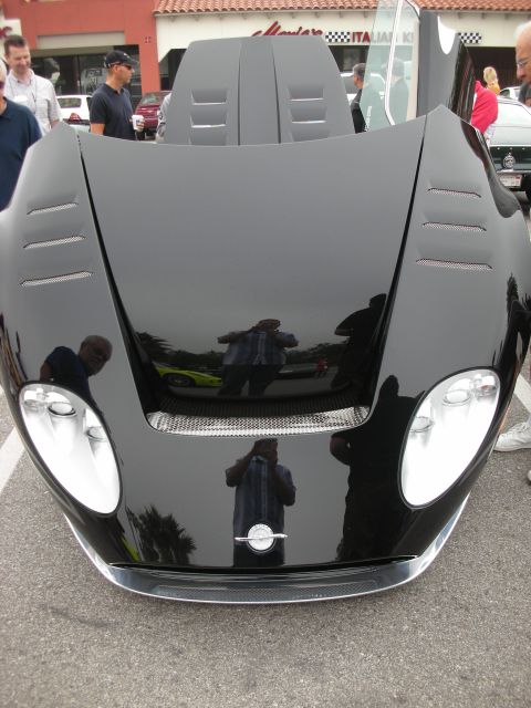 1998 Ford Crown Victoria - Head-on view of a black supercar with vented hood raised, its glossy surface reflecting bystanders at a car show.