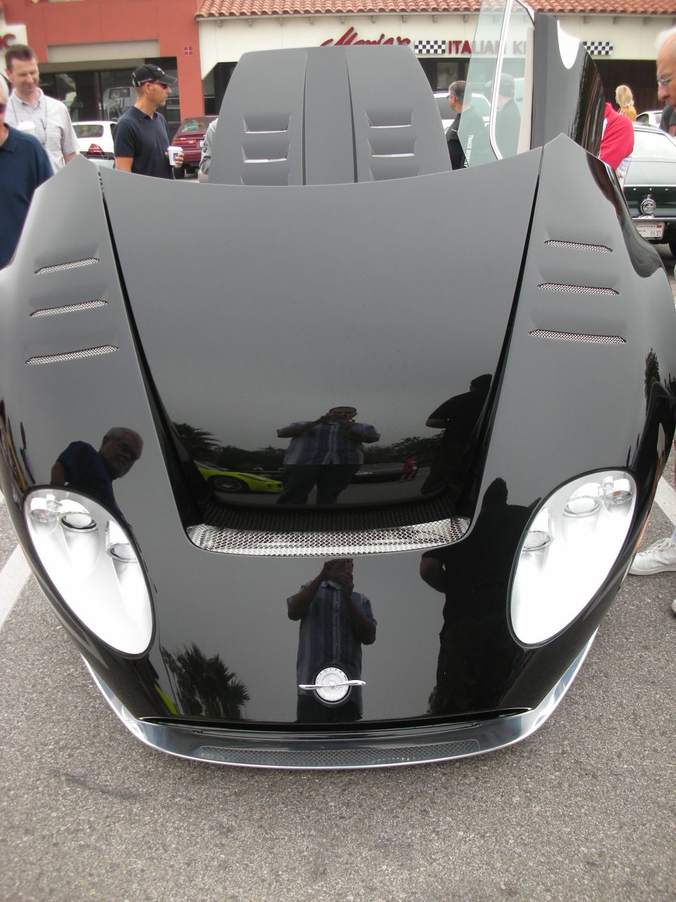 Front of black supercar with raised vented hood reflecting bystanders