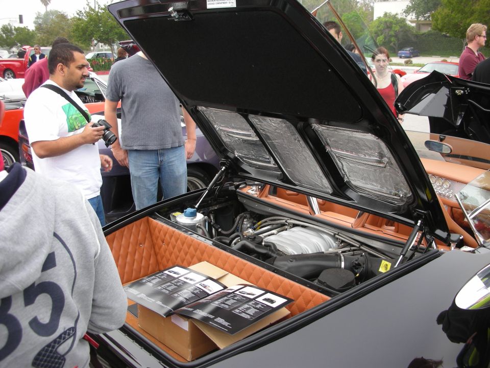 Open rear engine bay of black supercar with tan trim at car show