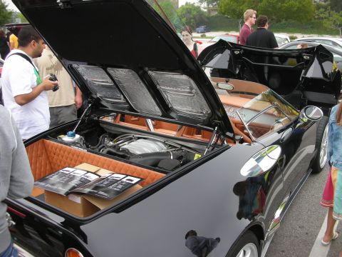 1998 Ford Crown Victoria - Rear three-quarter view of a black supercar with engine cover open and tan quilted interior, surrounded by show crowds.