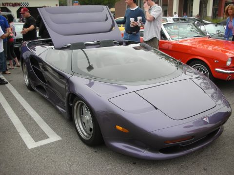 1998 Ford Crown Victoria - Front three-quarter view of a purple wedge-shaped supercar at a car show, with a red classic fastback Mustang nearby.