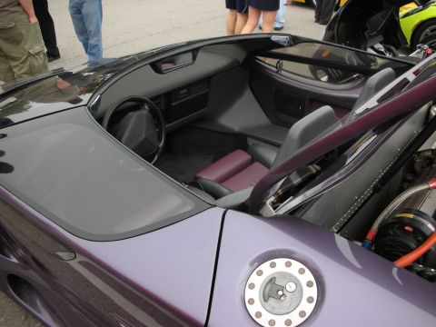 1998 Ford Crown Victoria - Open cockpit and aircraft-style fuel filler cap of a purple supercar with the rear engine bay exposed behind it.