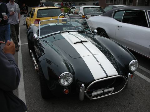 1998 Ford Crown Victoria - dark green Shelby Cobra roadster with twin white stripes shows its front grille and round headlights at a car meet.