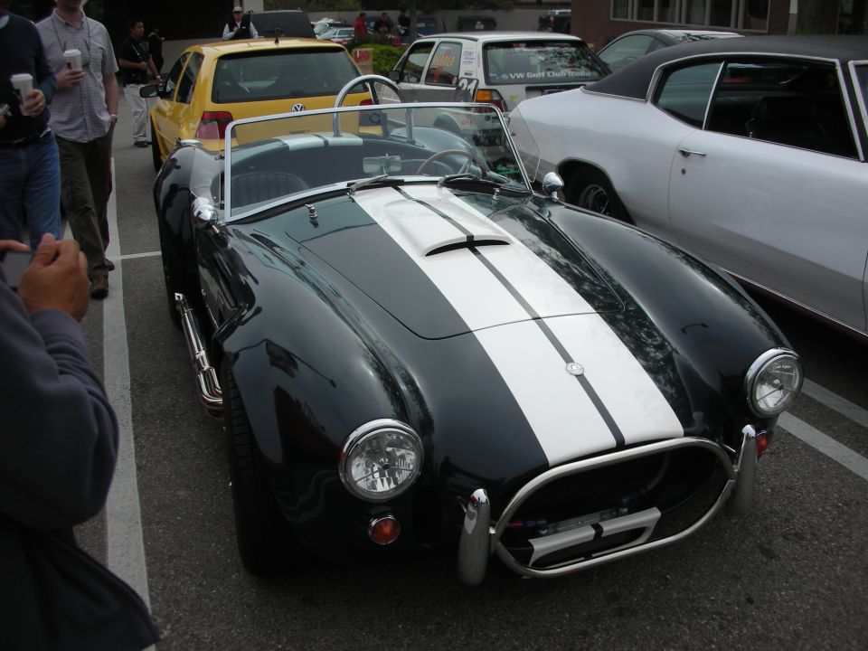 Front view of a dark green Shelby Cobra roadster with white stripes