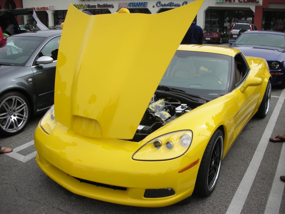 Yellow Chevrolet Corvette C6 with raised hood at a car show