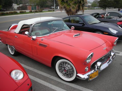 1998 Ford Crown Victoria - red classic Ford Thunderbird with white hardtop, wire wheels and whitewall tires is parked front three-quarter at a show.
