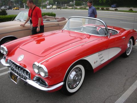 1998 Ford Crown Victoria - red first-generation Chevrolet Corvette roadster with whitewall tires sits front three-quarter as two men look on at a show.