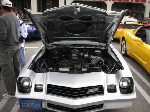 1998 Ford Crown Victoria - silver Camaro sits with its hood up showing the engine bay, wearing a Z28 front badge and a California plate, at an outdoor car show.