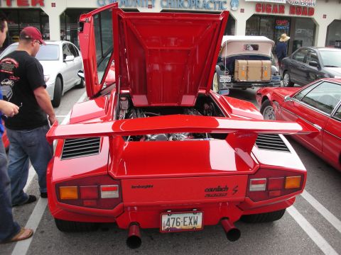 1998 Ford Crown Victoria - rear of a red Lamborghini Countach 5000 S with its rear wing and engine cover raised, showing tail lights and exhaust tips.