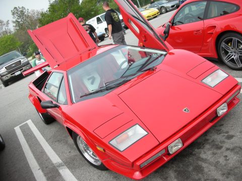 1998 Ford Crown Victoria - red wedge-shaped Lamborghini with its door and rear engine cover open, parked in a lot at a car show.