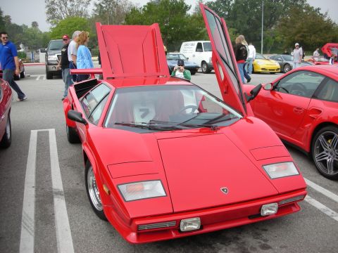 1998 Ford Crown Victoria - red Lamborghini Countach with its scissor door and rear engine cover open, parked among other cars and spectators.
