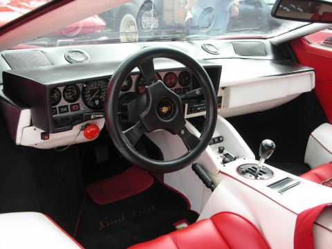 1998 Ford Crown Victoria - cockpit of a Lamborghini Countach showing the steering wheel, gauge cluster, white-and-red leather, and exposed gated shifter.
