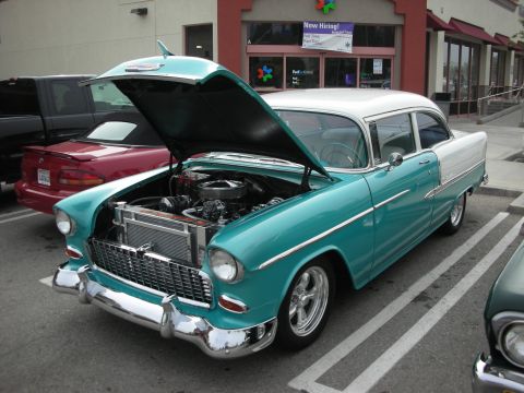 1998 Ford Crown Victoria - restored teal-and-white mid-1950s Chevrolet with chrome trim and open hood parked outside a storefront with a Now Hiring sign.