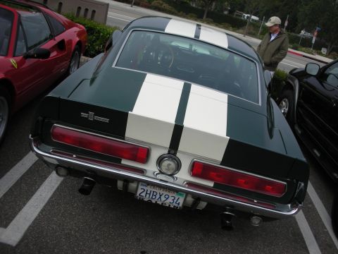 1998 Ford Crown Victoria - rear of a dark green fastback Mustang with twin white racing stripes and a California plate at an outdoor car show.