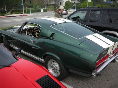 1998 Ford Crown Victoria - dark green 1960s Mustang fastback with white racing stripes parked near an intersection beside a black SUV.