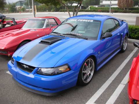 1998 Ford Crown Victoria - bright blue Ford Mustang Mach 1 coupe with a black hood scoop and chrome wheels parked at a car show.