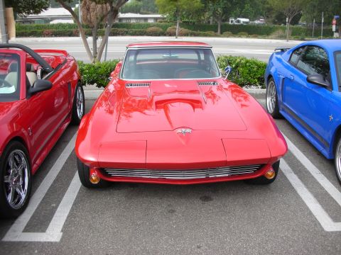 1998 Ford Crown Victoria - red mid-1960s Corvette Sting Ray seen head-on, parked between a red and a blue Mustang at an outdoor car show.