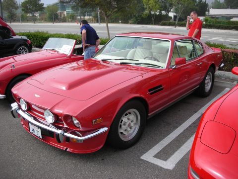 1998 Ford Crown Victoria - red Aston Martin V8 coupe with chrome bumpers and alloy wheels parked among other cars while people look on.