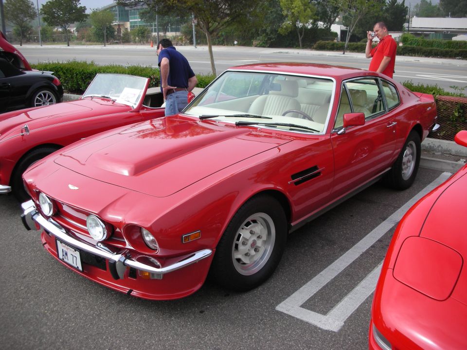 Red Aston Martin V8 coupe parked in a lot at a car show