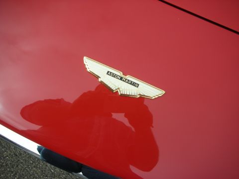 1998 Ford Crown Victoria - close-up of the gold and black Aston Martin winged emblem mounted on the glossy red bodywork of a car.