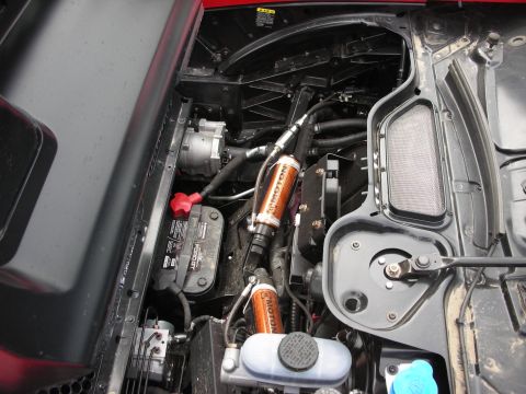 1998 Ford Crown Victoria - rear mid-engine bay showing a battery, coolant reservoir, black plumbing, and components with orange caps under an open lid.