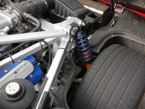 1998 Ford Crown Victoria - Close-up of a tuned engine bay showing a blue coilover spring, orange-bodied shock, a Ford-branded valve cover and a wide low-profile rear…