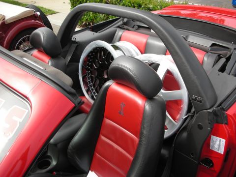 1998 Ford Crown Victoria - Interior of a red-and-black leather convertible with a roll hoop, two aftermarket wheels propped on the seats.