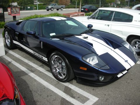 1998 Ford Crown Victoria - dark blue Ford GT supercar with white racing stripes and polished chrome wheels parked diagonally in a lot.