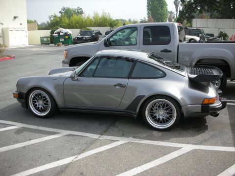 1998 Ford Crown Victoria - silver-grey Porsche 911 Turbo with a whale-tail spoiler and mesh wheels, shown in side profile in a parking lot.
