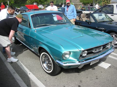 1998 Ford Crown Victoria - teal classic Ford Mustang fastback shown front three-quarter while a man crouches to inspect the front wheel at a meet.