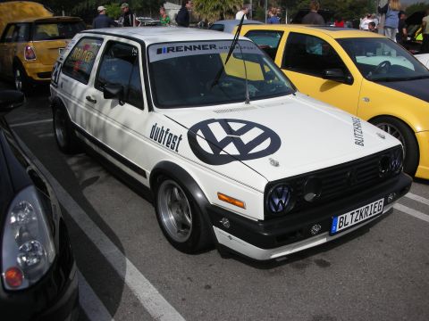 1998 Ford Crown Victoria - white Volkswagen Golf Mk2 covered in racing graphics including a large VW logo and 'dubfest' lettering, beside a yellow car.