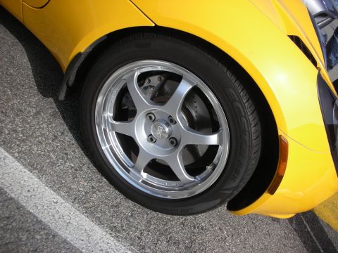 1998 Ford Crown Victoria - Close-up of a yellow car's front wheel fitted with a polished six-spoke alloy and a low-profile performance tire.