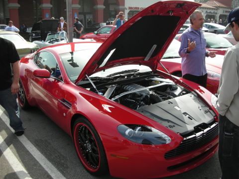 1998 Ford Crown Victoria - Front three-quarter view of a red Aston Martin V8 Vantage coupe with its hood raised, surrounded by onlookers at a car show.