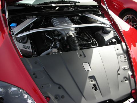 1998 Ford Crown Victoria - Engine bay of a red Aston Martin showing a polished strut tower brace and large black plastic engine covers.