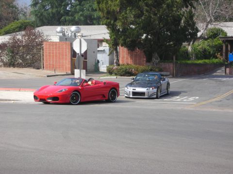 1998 Ford Crown Victoria - red Ferrari convertible and a silver tuner convertible parked at a suburban street corner near brick walls and trees.